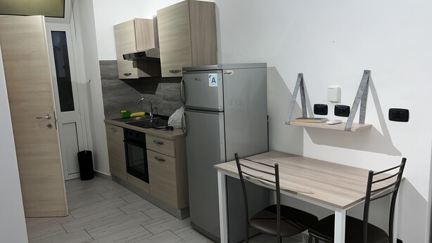 A compact kitchen with a built-in refrigerator, a small dining table, and a shelf with books and a phone. - Bed2Go Brescia (Turin)