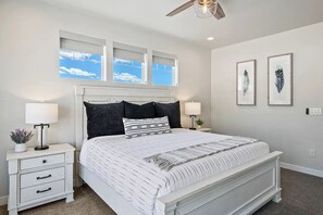 A bedroom with a bed, two bedside tables, a ceiling fan, and framed artwork on the wall.