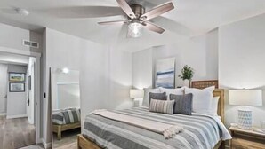 A bedroom with a bed, a nightstand, a ceiling fan, and a door leading to another room.