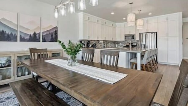 A modern kitchen with white cabinets, a wooden dining table, and a hanging light fixture.