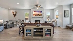 A spacious living room with a fireplace, a ceiling fan, and a large window.