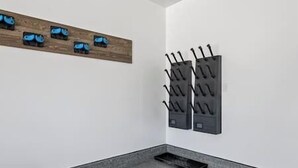 A corner of a room with a wooden shelf holding decorative items, a black wall-mounted rack with hooks, and a small black tray on the floor.