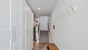 A narrow hallway with a wooden bench, white walls, and a staircase leading to another room.