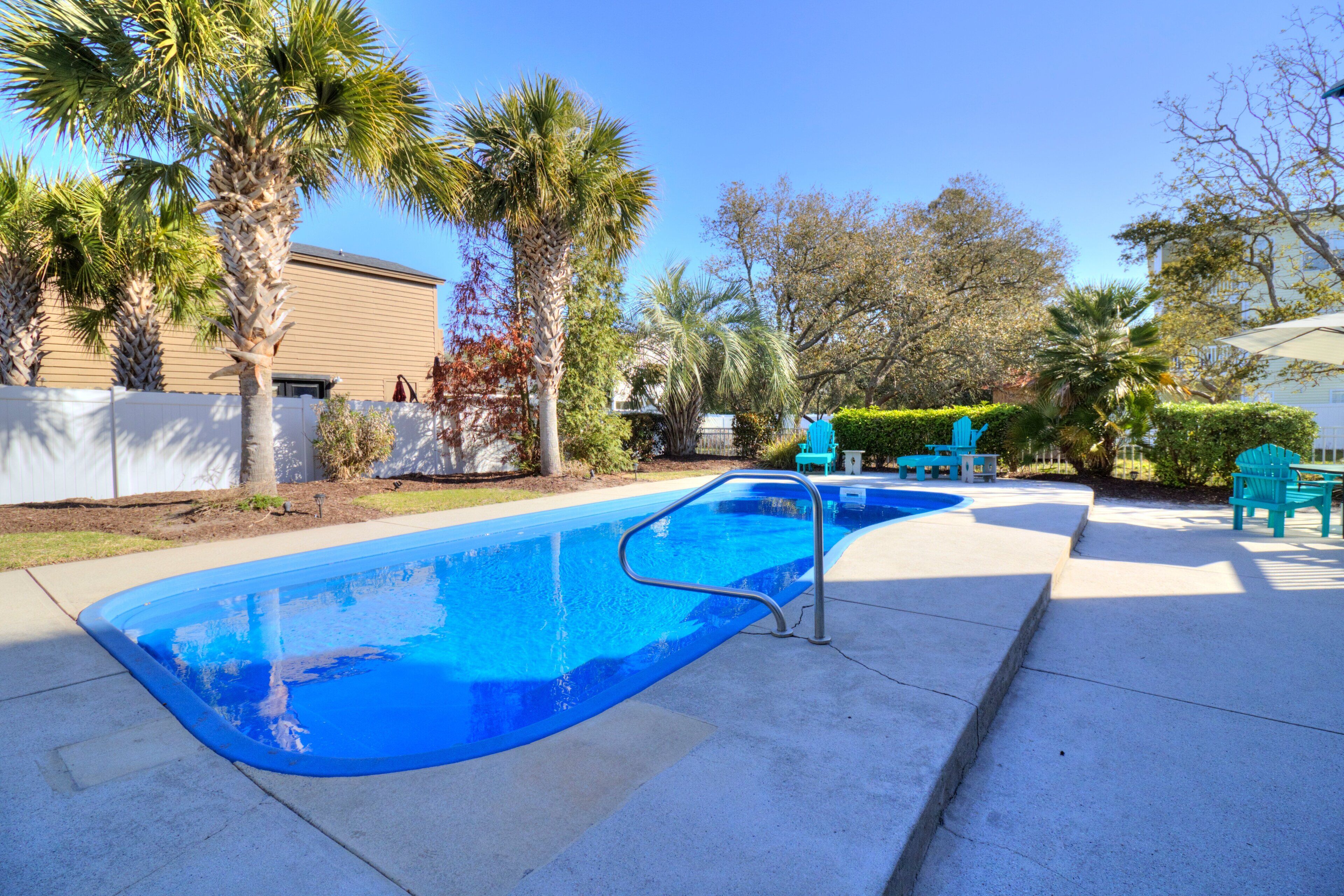A swimming pool with a metal ladder, surrounded by palm trees and a building in the background.