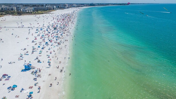 A beach with numerous umbrellas and people, a lifeguard tower, and a clear view of the ocean.