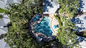An aerial view of a residential area with a swimming pool surrounded by trees and a patio area with lounge chairs.