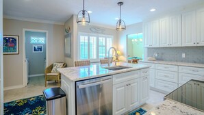 A modern kitchen with white cabinets, a stainless steel dishwasher, and pendant lighting.