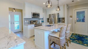 A kitchen with white cabinets, stainless steel appliances, a marble countertop, and wicker bar stools.