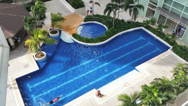 Una gran piscina de disseny corbat, envoltada de palmeres i un edifici.
