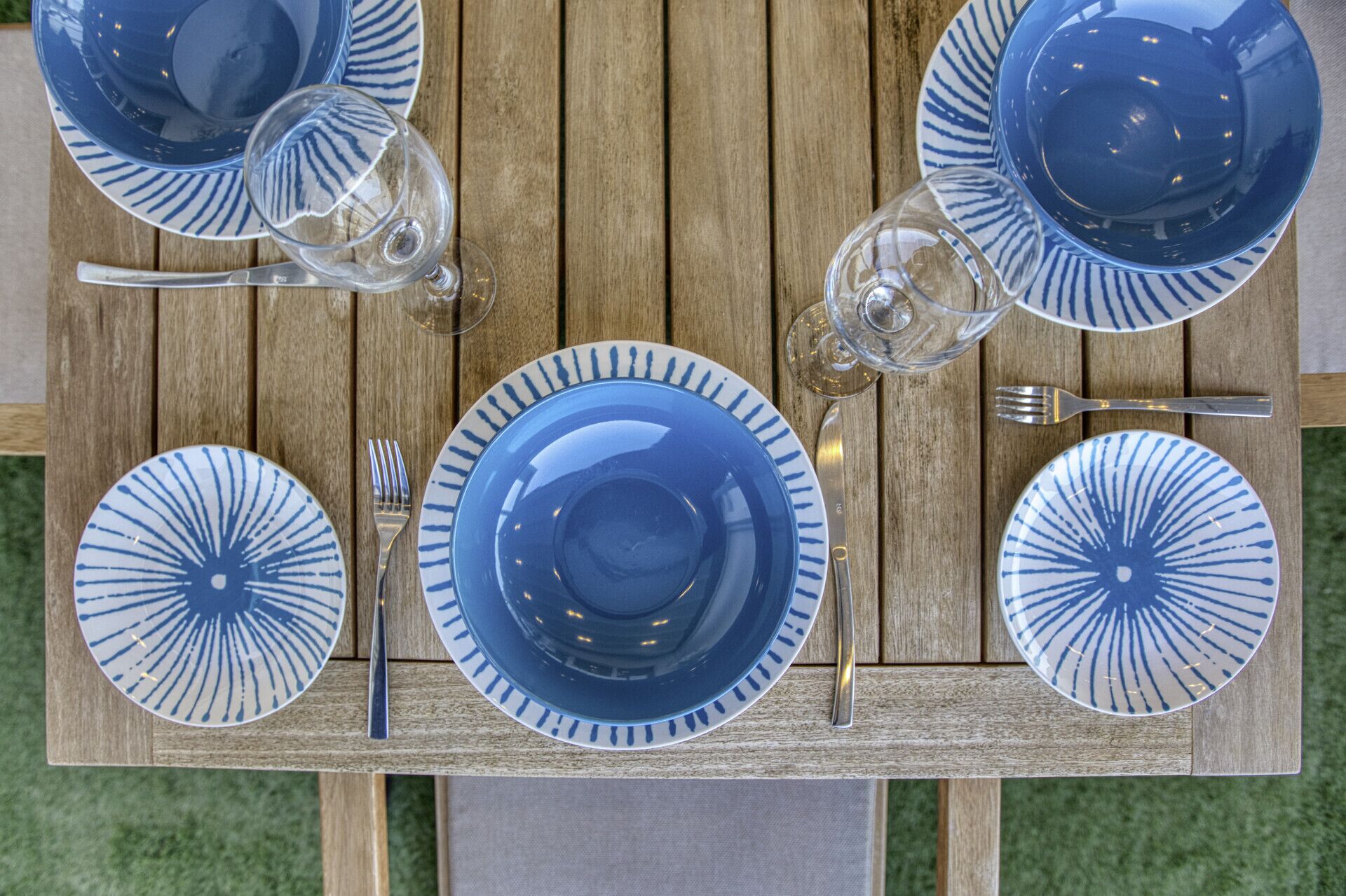 A wooden table set with blue and white plates, a fork, a knife, and two wine glasses.