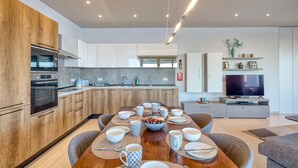 A modern kitchen with built-in appliances, a dining area with a wooden table set for four, and a TV in the living area. - Beautiful Penthouse with pool and terrace (Is-Swieqi)