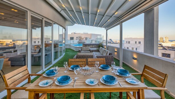 A rooftop terrace with a dining table set for six, surrounded by wicker furniture, and overlooking a cityscape. - Beautiful Penthouse with pool and terrace (Is-Swieqi)