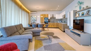 A modern living room with a sofa, a dining area with chairs, a kitchen with a stove and cabinets, and a TV on a stand. - Beautiful Penthouse with pool and terrace (Is-Swieqi)