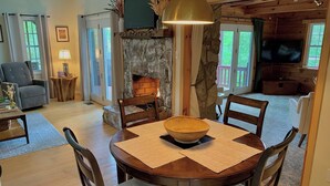 Ein gemütliches Wohnzimmer mit Kamin aus Stein, einem Esstisch mit Stühlen und einem Fernseher im Hintergrund.