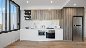 A modern kitchen with a built-in oven, microwave, and refrigerator, a marble backsplash, and a wooden accent wall.