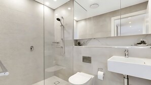 A modern bathroom with a glass shower enclosure, a white toilet, and a sink with a mirror above it.
