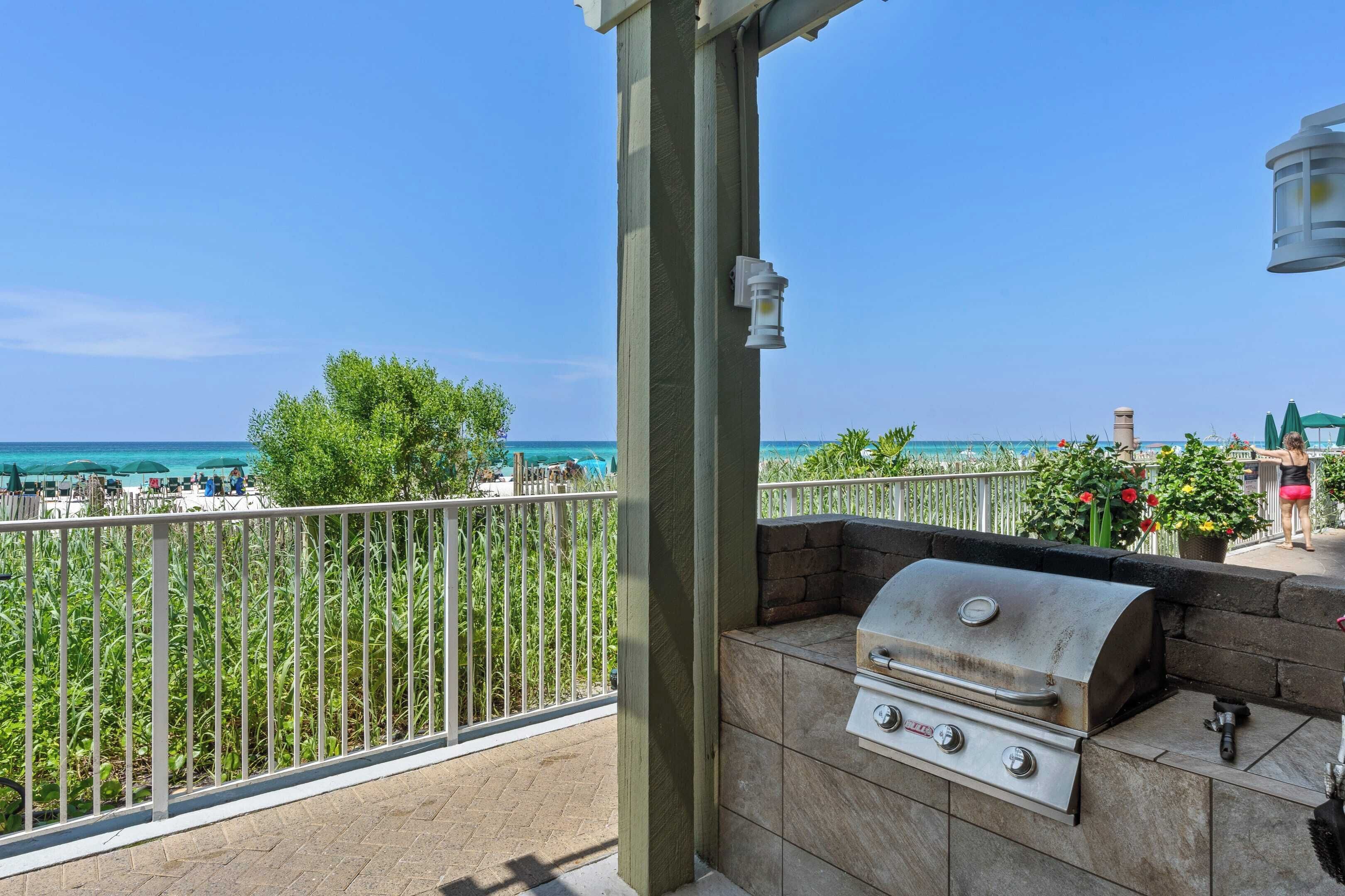 Un patio exterior con una parrilla, vistas a la playa y una barandilla.