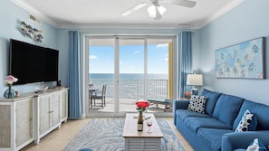 A living room with a TV, sofa, coffee table, and a view of the ocean.