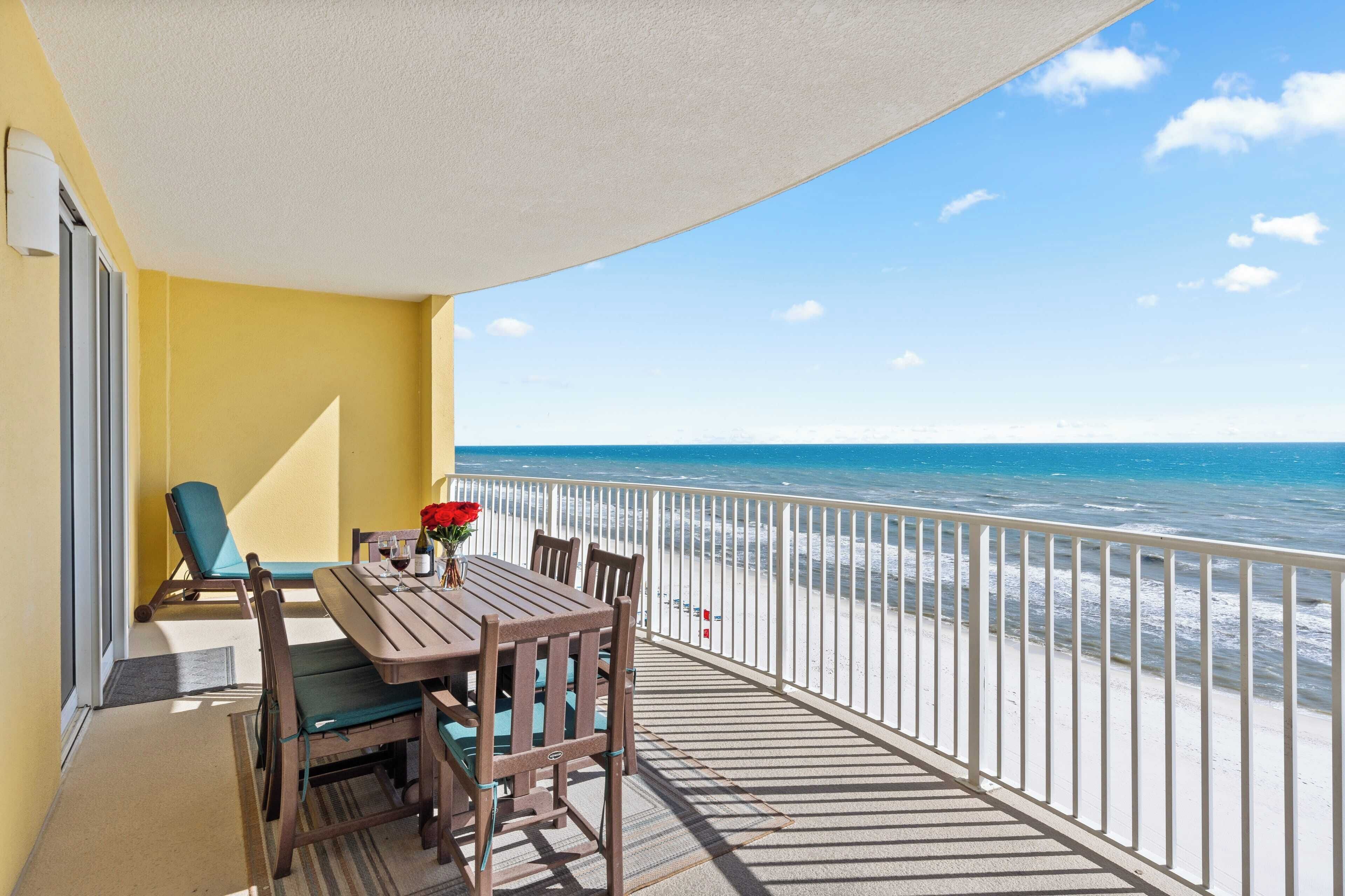 A balcony with a wooden table and chairs, a chair with a cushion, and a view of the ocean.