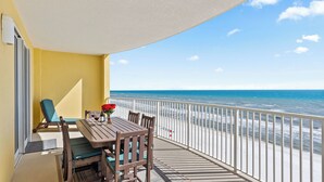 A balcony with a wooden table, chairs, and a vase of red flowers. - Beachfront Condo w/ Ocean Views + Pool Access + Beach Gear Emerald Isle 808 by Avantstay (Panama City Beach)