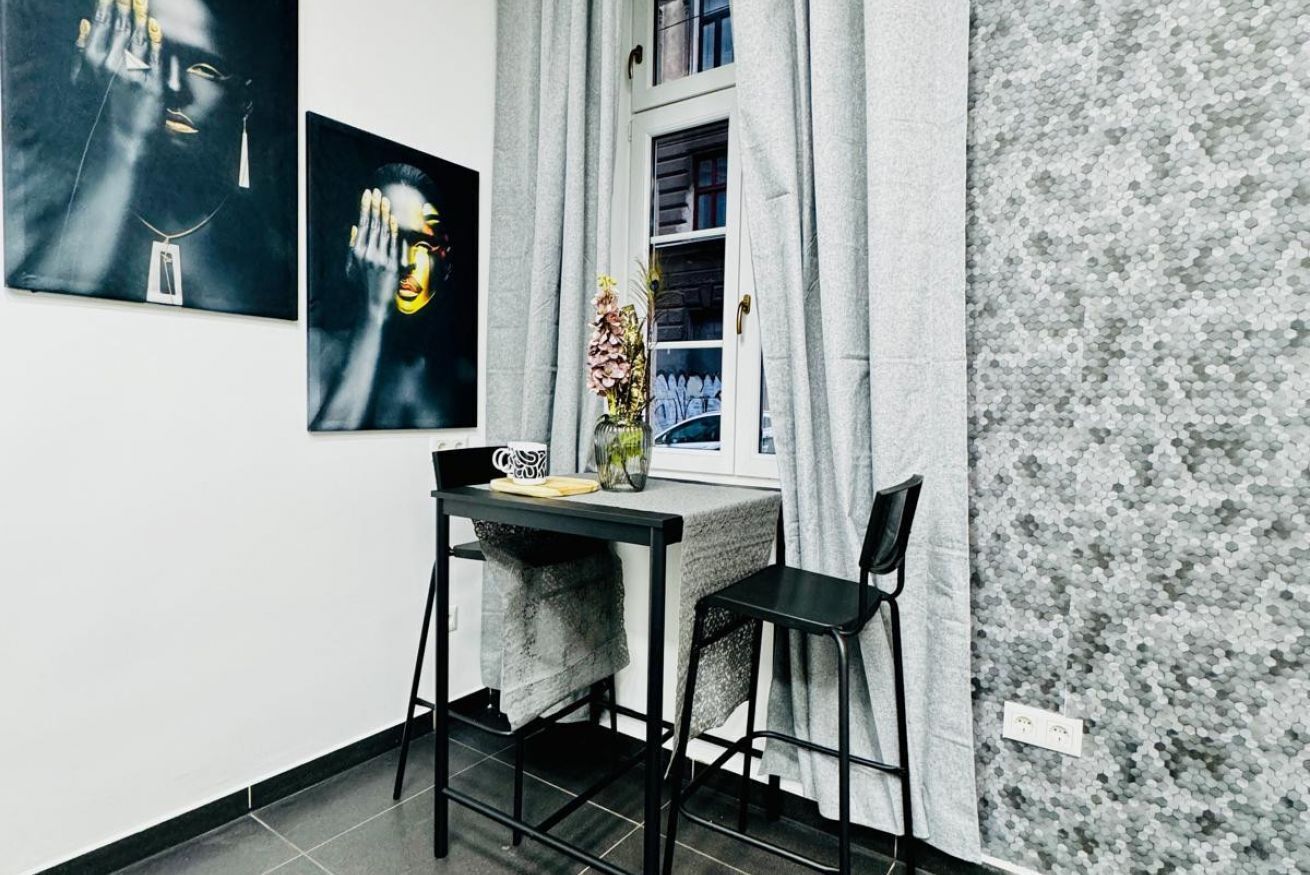 Un pequeño comedor con una mesa y dos sillas, un florero con flores y dos obras de arte colgadas en la pared.