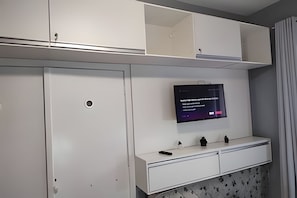 A room with a TV mounted on the wall, a white cabinet with drawers, and a small shelf with decorative items. - Quartos Prox Av Paulista e Frei Caneca (Sao Paulo)