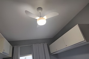 Un ventilador de techo con lámpara, una ventana con cortinas y armarios blancos.