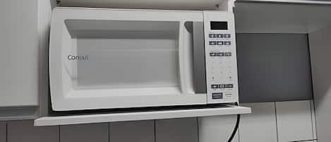 A white microwave oven with a digital control panel, mounted on a white wall with a tiled backsplash.