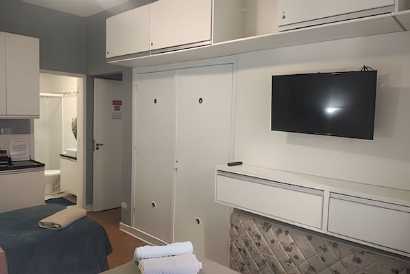 Habitación de hotel con cama, televisión montada en la pared, baño con ducha y zona de escritorio.