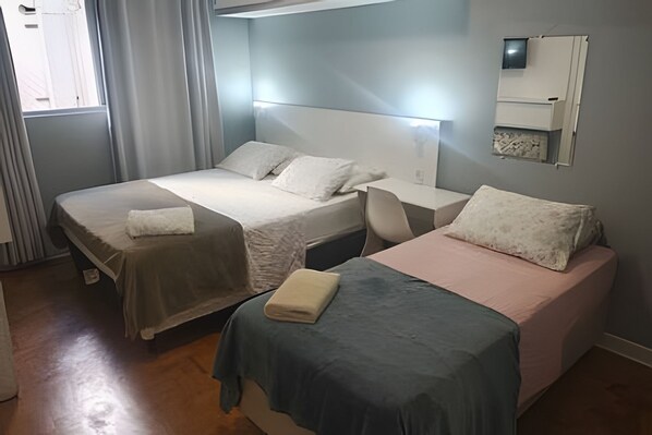 Hotellihuone, jossa on kaksi sänkyä, työpöytä, tuoli, peili ja ikkuna, jossa on verhot.
