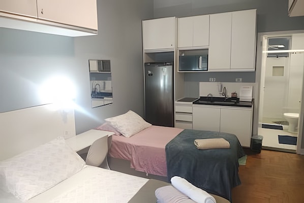A compact hotel room with a bed, a small desk, a kitchenette, and a bathroom.