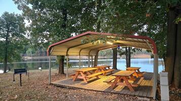 Un espace pique-nique abrité, doté de bancs et d’un abri situé au bord d’un lac.
