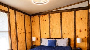 Un dormitorio con pared de madera, una cama con cubrecama azul, dos lámparas de noche y una lámpara de techo.