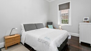 A bedroom with a bed, nightstand, dresser, window, and chandelier.