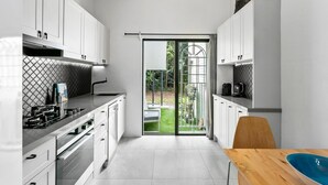 A modern kitchen with white cabinets, a gas stove, and a dining area with a wooden table and blue bowl.