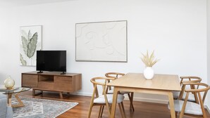 Ett modernt matområde med ett träbord, sex stolar, en tv placerad på ett träskåp och två abstrakta konstverk på väggen.
