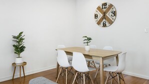 Un comedor con una mesa de madera, sillas blancas, una planta en maceta y un reloj de pared.