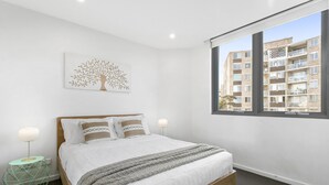 Un dormitorio moderno con una cama grande, vistas de un edificio a través de una ventana y una obra de arte con motivos de árboles en la pared.