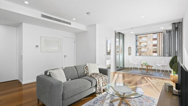 Una sala de estar moderna con un sofá gris, una mesa de centro de vidrio y piso de madera.