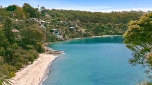 Una zona costera con playa de arena, agua azul cristalina y edificios residenciales en una colina.