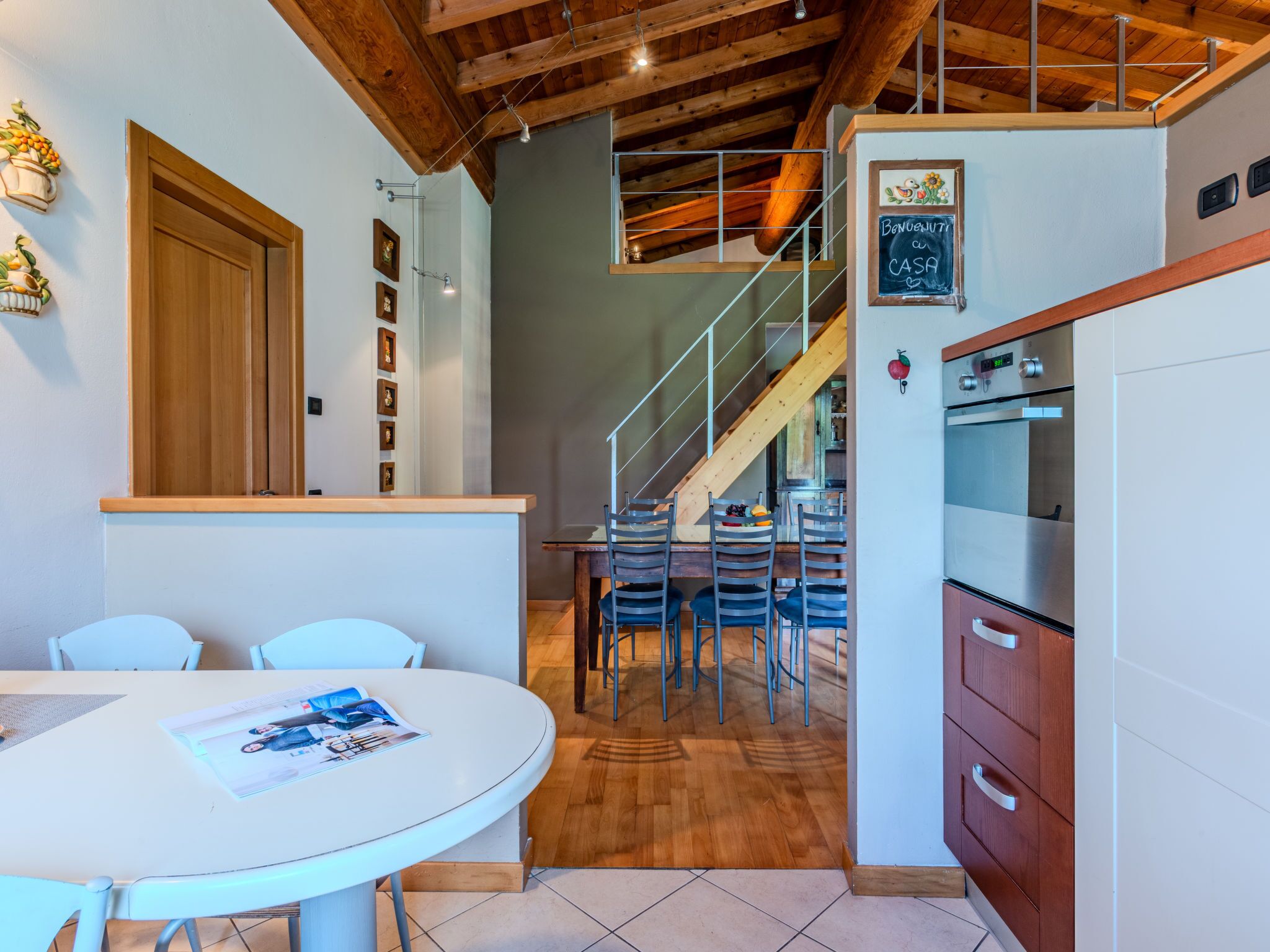 A modern kitchen with a wooden ceiling, a dining area with a round table, and a staircase leading to an upper level.
