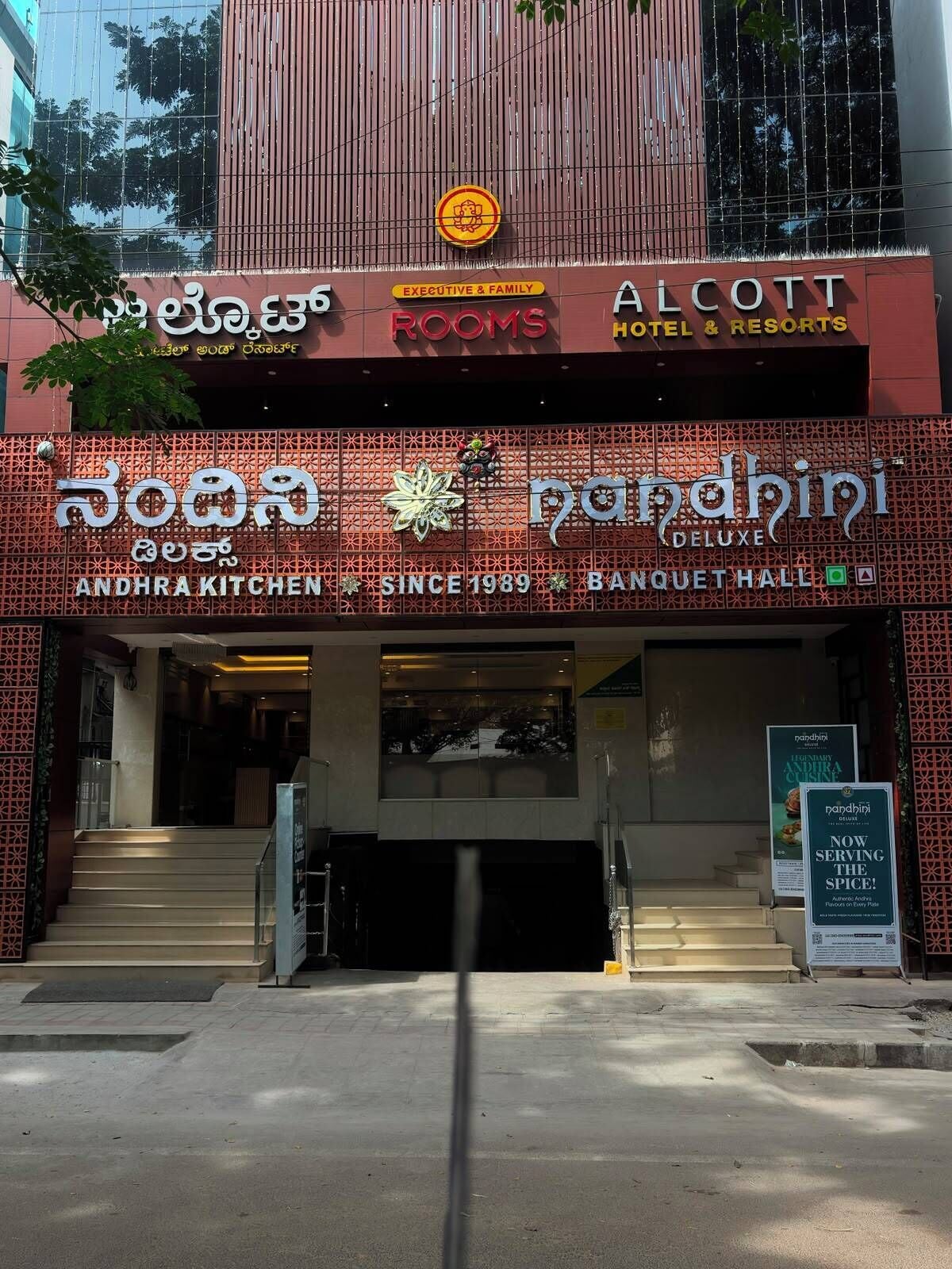 Ein Gebäude mit Hinweisschildern für 'ALCOOTT HOTEL & RESORTS' und 'Nandhini DELUXE BANQUET HALL'.