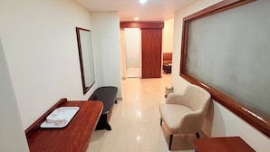 A hotel room with a wooden desk, a chair, a sofa, and a large window.