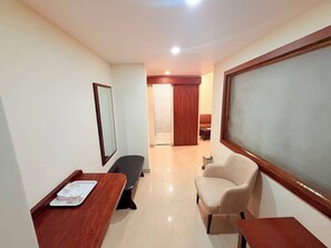Habitación de hotel con escritorio de madera, una silla, un sofá y un ventanal grande.