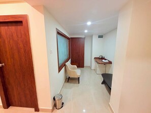 Un pasillo con puerta de madera, un espejo enmarco, una pequeña zona de estar, una kitchenette y un bote de basura.