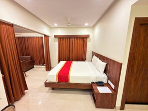 A hotel room with a large bed, wooden headboard, a bedside table with a phone, and a door to a sitting area. - Alcott Hotel & Resorts (Bengaluru)