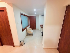 A hallway with a wooden door, a white chair, a small table, and a trash bin.