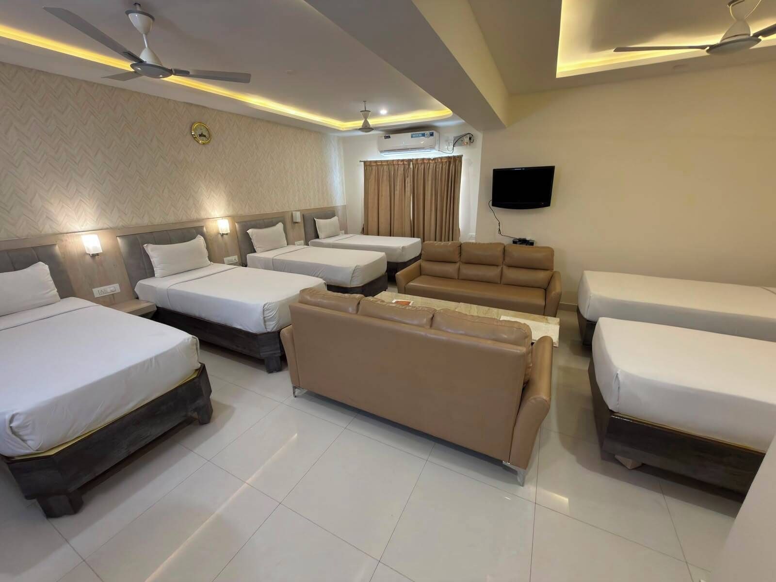 Une chambre d’hôtel avec trois lits, un canapé, un téléviseur à écran plat et un ventilateur de plafond.