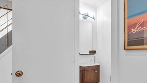 A bathroom with a white wall, a wooden cabinet, a mirror, and a sink.