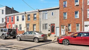 A row of townhouses with a garage, a red car, and a silver car parked in front.